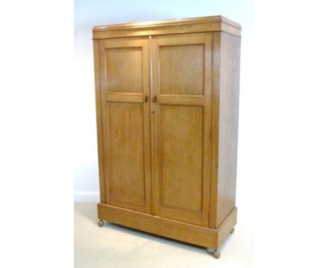 An Art Deco oak gentleman's wardrobe with caddy top, twin panel doors with drop handles, enclosing a hanging space and three 