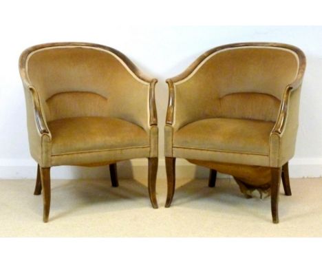 A pair of Edwardian tub Bath chairs with beech frames, curved back rails, raised on outswept legs, upholstered in light brown