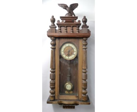 A Vienna wall clock in a walnut case, with eagle crest, the white ceramic face with Roman numerals, 92 by 35 by 16cm. 