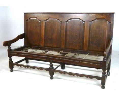 A late 17th century oak long settle, with four panel back rest, shaped open arms, raised on knop turned front supports joined
