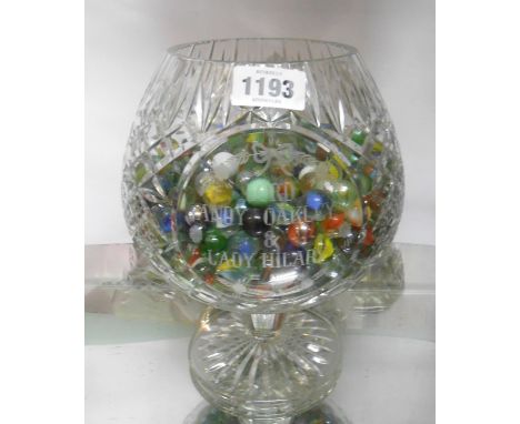 A cut crystal goblet containing a quantity of vintage marbles