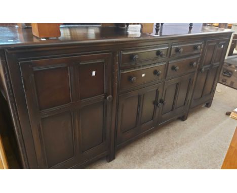 A 2.1m vintage Ercol dark elm sideboard with four central drawers, double cupboard under and flanking cupboard doors, set on 