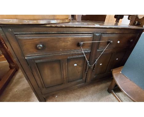 A 1.27m vintage Ercol dark elm sideboard with cutlery and other drawer over pair of panelled cupboard doors, set on block fee