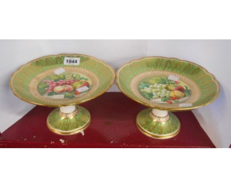 A pair of 19th Century porcelain dessert comports with central hand painted fruit decorated panel on a green ground with gilt