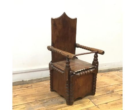 A vernacular 19thc oak child's commode, the shield shaped back enclosed by bobbin arms above a hinged seat, above a panel fro