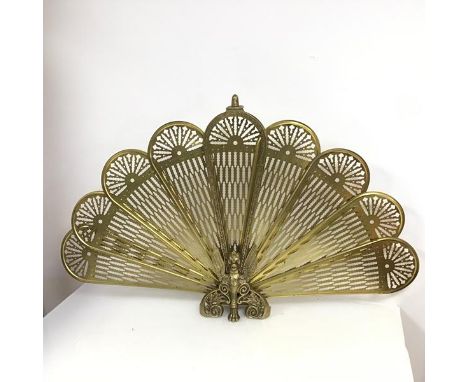 A brass metamorphic peacock feather style firescreen with nine folding panels, folding above a winged beast with single paw f