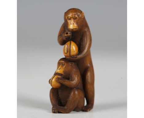 A Japanese carved and stained ivory okimono netsuke, Meiji period, finely modelled as two monkeys, each holding a fruit or nu