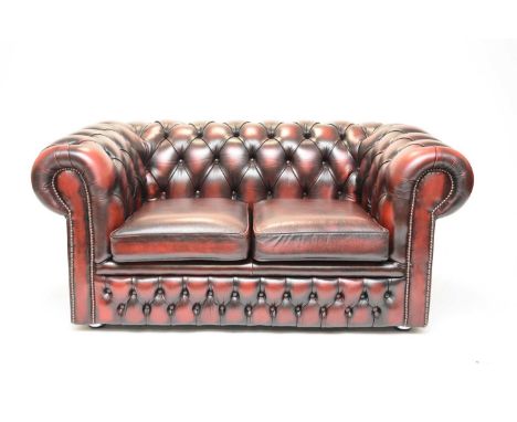 A leather Chesterfield two-seater sofa, late 20th century, of typical button-back scroll-arm form, in a deep red 'antiqued' h