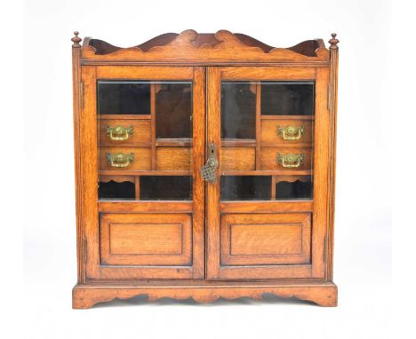 An Edwardian oak smokers cabinet, the shaped pediment above twin glazed doors, opening to a series of drawers and pigeon hole