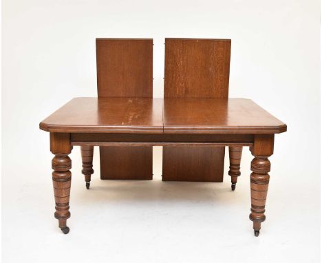 An Edwardian oak wind-out extending dining table, the moulded top with canted corners on a plain frieze, raised on turned sup