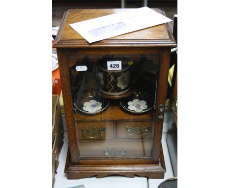 AN OAK SMOKER'S CABINET, with front opening glazed door, with ceramic tobacco jar (re-glued lid) and two ceramic dishes (one 