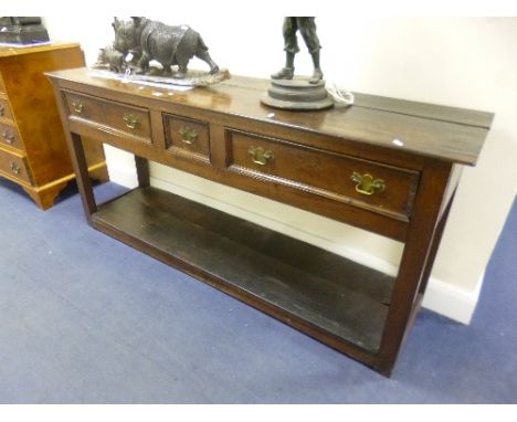 A GEORGIAN OAK THREE DRAWER DRESSER BASE, the small central drawer flanked by larger drawers, on square supports with lower s