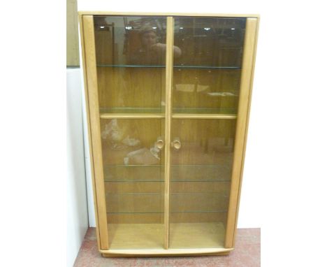 Ercol beech and elm display cabinet, with twin glazed doors enclosing wooden and glass shelves, the interior fitted for elect