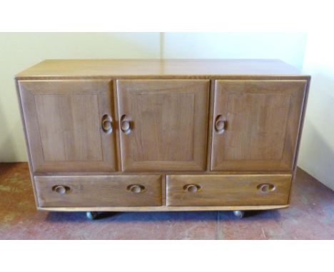 Mid-century Ercol 'Windsor' range elm sideboard with three cupboard doors above two short drawers, on castors, 76cm high, 129
