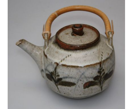 Manner of Bernard Leach, a stoneware studio pottery teapot and cover, with cane handle, decorated with abstract leaf forms. 1