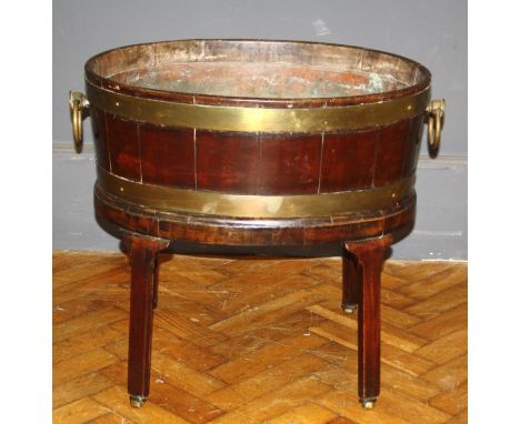 A George III mahogany and brass band oval open wine cooler, having ring handles and raised on square tapered legs and brass c