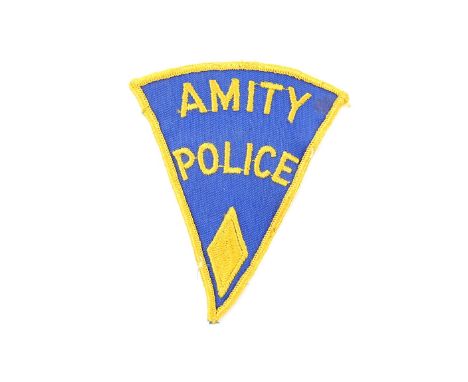 Jaws (1975) - ‘Amity Police’ Uniform Patch.Triangular cotton costume patch, bearing ‘Amity Police’ embroidered centrally, &am