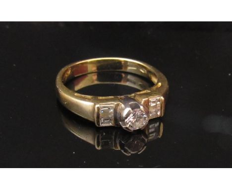 A gold ring with central round cut diamond flanked by diamond baguettes, stamped 750. Size J/K, 3.5g