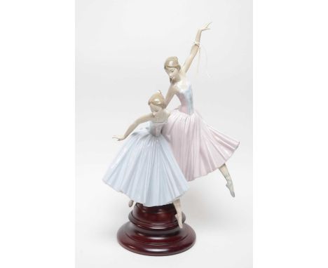 A Lladro ceramic figure group of two ballerinas, raised on a stained wood stepped circular base, 49cms high overall.