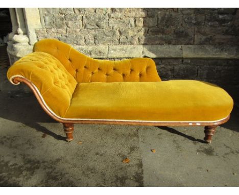 A Victorian walnut chaise lounge with mustard coloured upholstered seat, scrolled button back, raised on turned supports and 