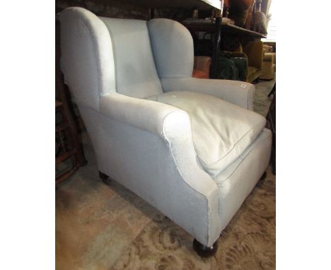 An Edwardian wing armchair with shaped outline, light blue ground upholstery, loose feather filled seat cushion and raised on