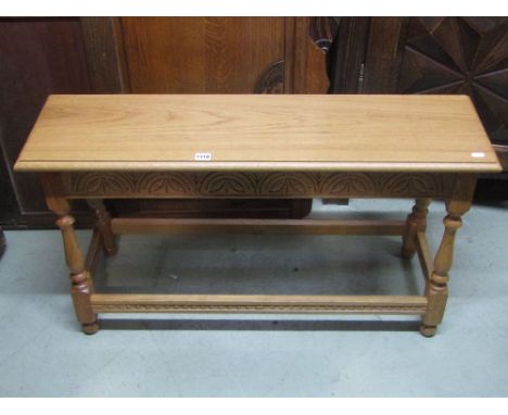 An Old English style light oak bench stool with carved frieze, turned supports and moulded stretchers, 102 cm long 