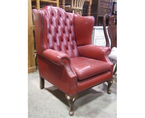 A Queen Anne style wing armchair with shaped outline and orangey red leather upholstery with button back and studded detail, 