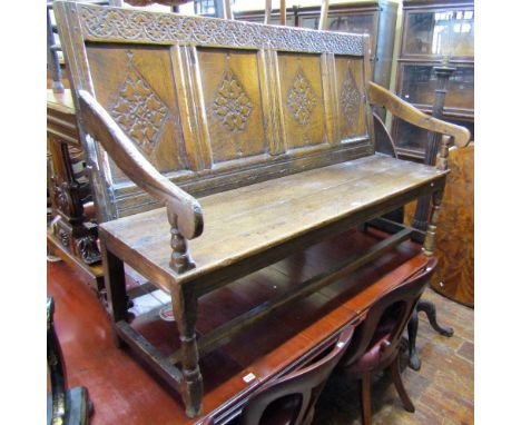 An antique oak settle the full panelled back with lozenge shaped detail, beneath a repeating trailing floral frieze with scro