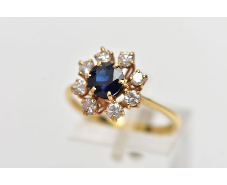 AN 18CT YELLOW GOLD SAPPHIRE AND DIAMOND CLUSTER RING, centering on a circular cut blue sapphire, in a six claw setting, with