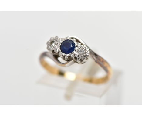 A YELLOW METAL CROSS OVER THREE STONE RING, designed with a central circular cut blue sapphire, flanked with illusion set rou