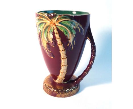 A Beswick water jug decorated with a palm tree on a rouge ground, model no. 1068, h. 23 cm, together with a smaller jug in th