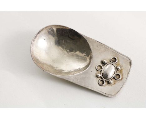 AN ARTS &amp; CRAFTS HANDMADE CADDY SPOON with a hammered finish, an egg-shaped bowl and a lug handle with an applied decorat