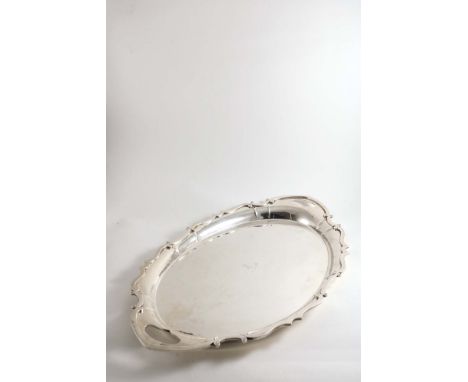 AN EDWARDIAN TWO-HANDLED TRAY  of shaped oval outline with an applied scroll border, button feet and a central, engraved cres