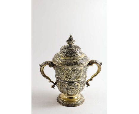 A GEORGE II SILVERGILT REPOUSSE-WORK CUP &amp; COVER with twin, leaf-capped scroll handles, a campana shaped body &amp; a mou