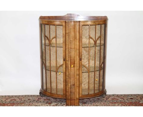 An Art Deco figured walnut ledge back demi-lune double door glazed display cabinet, having twin interior glass shelves, width