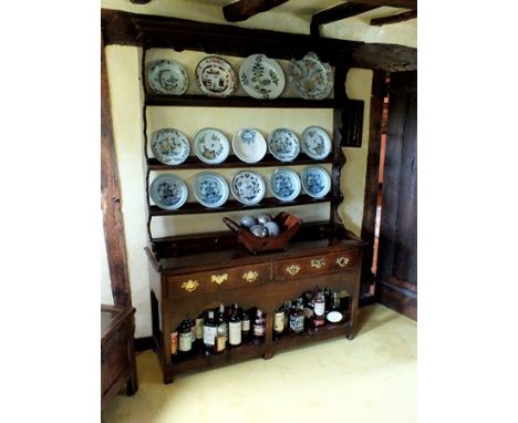 An 18th century oak high dresser, the superstructure with moulded cornice, undulating frieze, four open back plate rails, ser