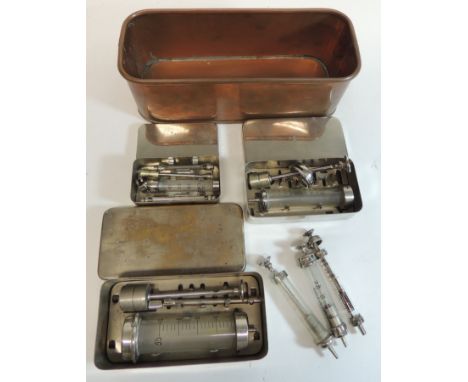 Three steel containers each containing hypodermic syringes; three loose syringes and a small copper sterilising trough