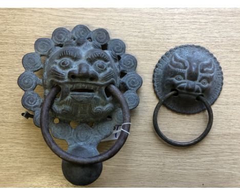 A Chinese metal ware ornate door knocker modelled as the face of a temple dog, height 21 cm, together with another smaller.  