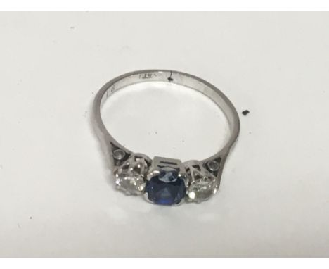 A platinum ring set with a good coloured sapphire flanked by brilliant cut diamonds. Ring size O.