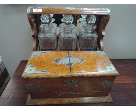 A late Victorian/Edwardian golden oak tantalus having three glass decanter divisions and box front