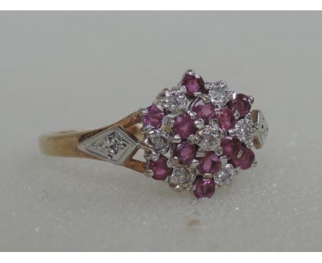 A ladies dress ring having a ruby and diamond cluster in a raised basket mount with diamond chips to shoulders on a 9ct gold 