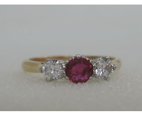 A ladies dress ring having a central ruby flanked by two diamonds, approx .25ct in a raised claw mount on a yellow metal loop