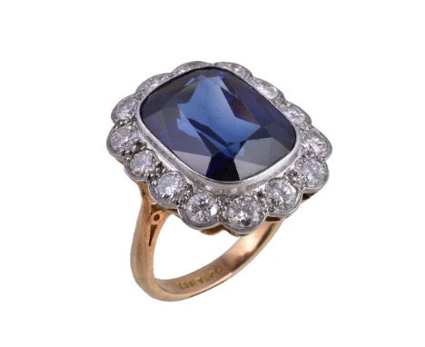 A synthetic sapphire and diamond ring, the cushion cut synthetic sapphire collet set within a surround of brilliant cut diamo