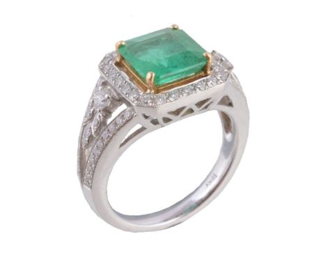 An emerald and diamond dress ring, the central step cut emerald in a four claw setting, within a surround of brilliant cut di