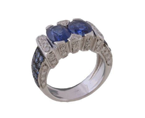 A sapphire and diamond ring, the two oval cut sapphires within a brilliant cut diamond set surround, the shoulders set with c