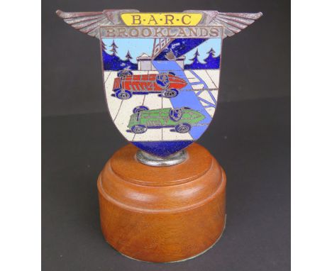 An enamelled Brooklands car badge depicting a green and red racing cars, of shield form and with traces of chrome, Stamped on