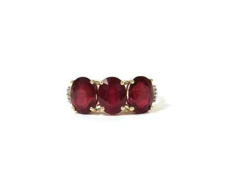A gold three stone fracture filled ruby ring, with diamond set shoulders, a row of three oval mixed cut fracture filled rubie