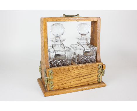 A two-bottle tantalus, two cut glass spirit decanters in oak tantalus with locking pin, each bottle with a silver decanter la