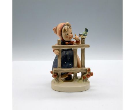 A matte hand painted figure of a little girl wearing a polka dot dress and head scarf, talking to a bird perched on a fence. 