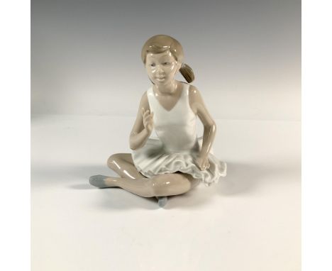 A glossy figure of a ballerina who is speaking and she is sitting down with her legs crossed. Nao by Lladro backstamp. Artist